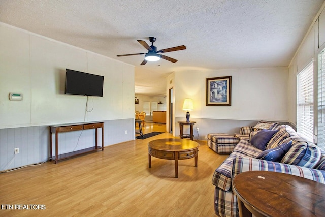 living room with ceiling fan, light hardwood / wood-style flooring, and a textured ceiling