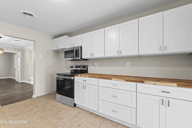 kitchen with wooden counters, appliances with stainless steel finishes, white cabinets, and light tile patterned floors