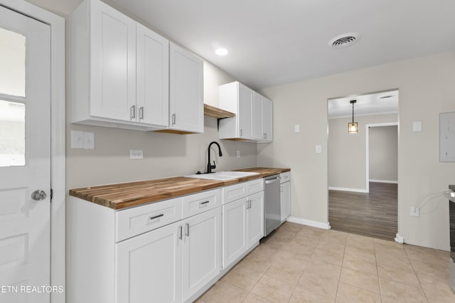 kitchen featuring stainless steel dishwasher, sink, white cabinetry, hanging light fixtures, and butcher block counters