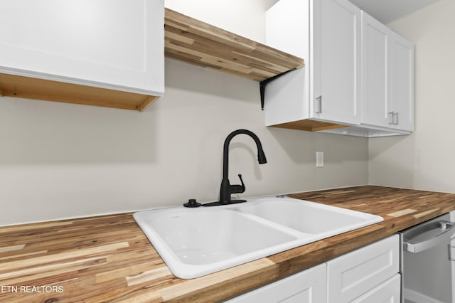 kitchen with stainless steel dishwasher, white cabinetry, sink, and wooden counters