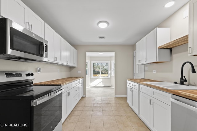 kitchen featuring sink, butcher block countertops, light tile patterned flooring, white cabinetry, and stainless steel appliances