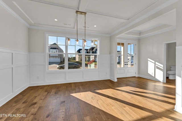 unfurnished dining area with crown molding, wood-type flooring, a wainscoted wall, and a decorative wall