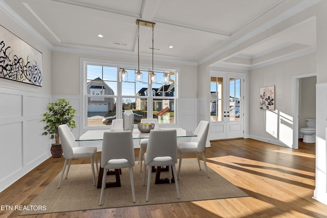 dining area featuring a decorative wall, wainscoting, wood finished floors, and crown molding