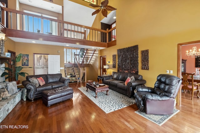 living room featuring hardwood / wood-style floors, a towering ceiling, and ceiling fan with notable chandelier