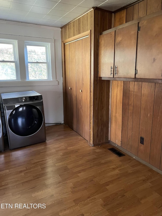 laundry room featuring wood walls, cabinets, wood-type flooring, and washer / clothes dryer