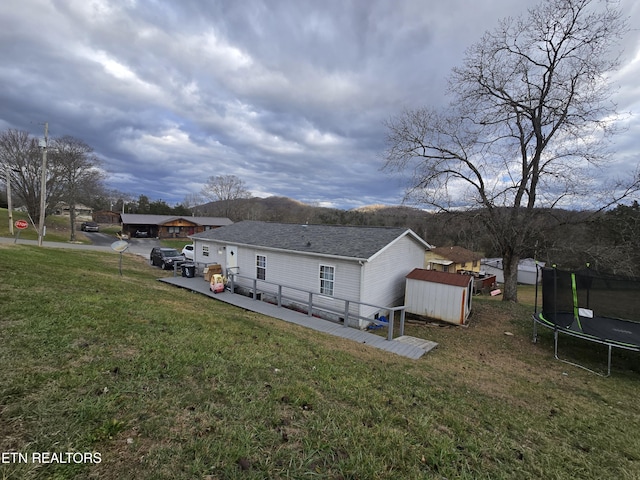 back of property with a lawn, a storage shed, and a trampoline