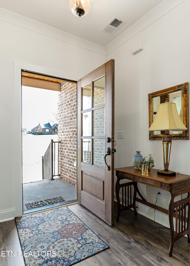 foyer entrance featuring dark hardwood / wood-style flooring, ornamental molding, and brick wall