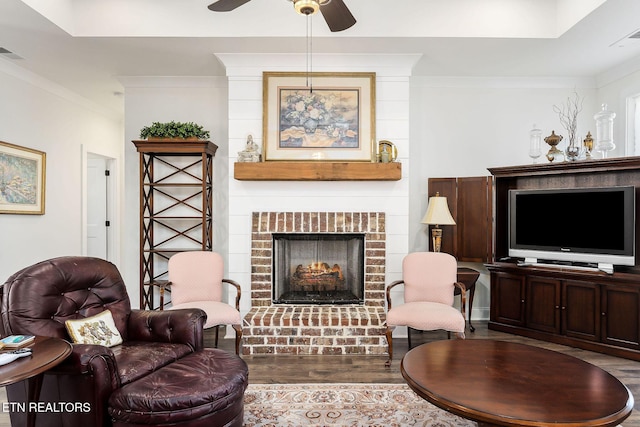 sitting room featuring hardwood / wood-style flooring, ceiling fan, ornamental molding, and a brick fireplace