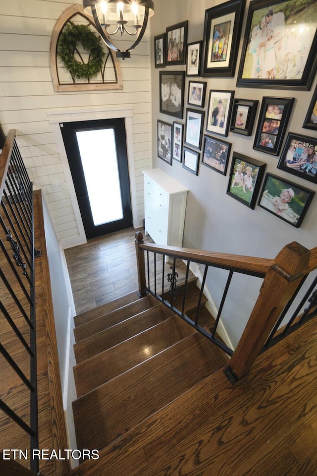 stairway featuring wood walls, hardwood / wood-style floors, and a chandelier