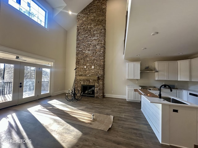 unfurnished living room featuring a towering ceiling, dark wood-type flooring, french doors, a stone fireplace, and sink