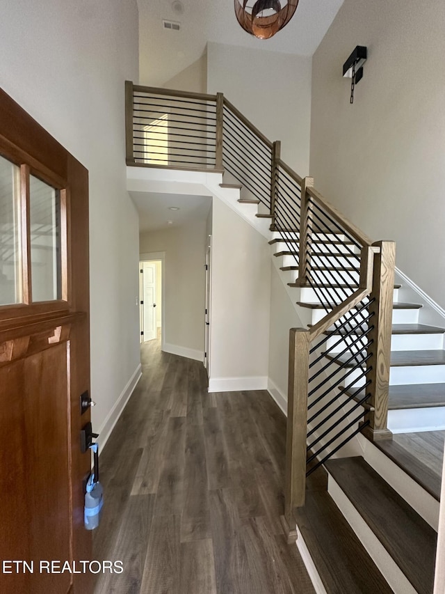 entryway featuring dark wood-style flooring, visible vents, a towering ceiling, baseboards, and stairs