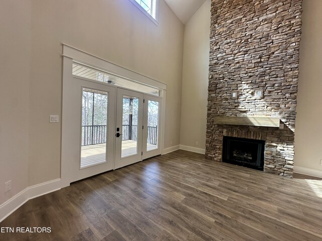 unfurnished living room featuring high vaulted ceiling, wood finished floors, french doors, a fireplace, and baseboards