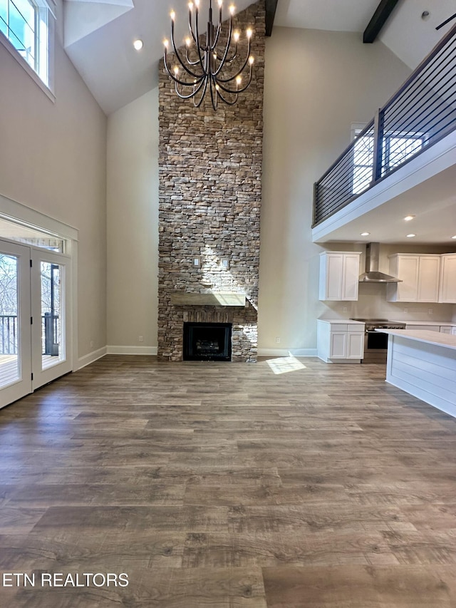 unfurnished living room with beam ceiling, baseboards, a stone fireplace, and wood finished floors