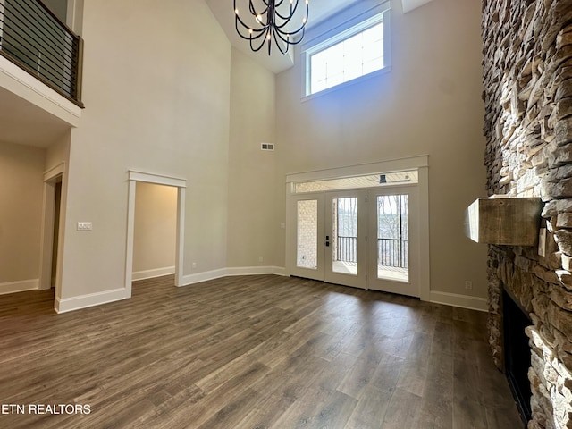 unfurnished living room featuring visible vents, baseboards, dark wood finished floors, a stone fireplace, and an inviting chandelier