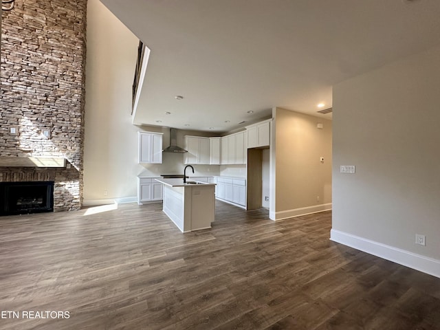 kitchen with wall chimney range hood, open floor plan, dark wood-style flooring, and a sink