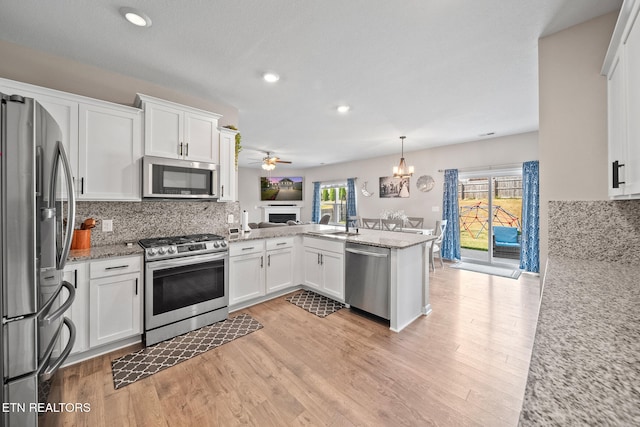 kitchen with kitchen peninsula, appliances with stainless steel finishes, backsplash, pendant lighting, and white cabinetry