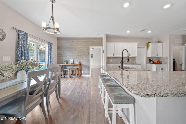 kitchen featuring an inviting chandelier, light stone counters, backsplash, decorative light fixtures, and white cabinets