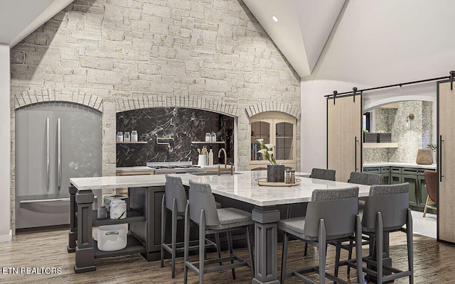 dining area featuring a barn door, wood-type flooring, sink, and high vaulted ceiling