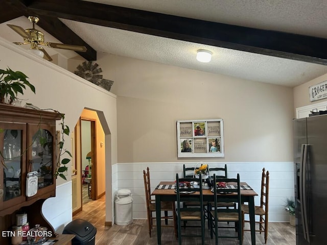 dining area with wood-type flooring, a textured ceiling, lofted ceiling with beams, and ceiling fan