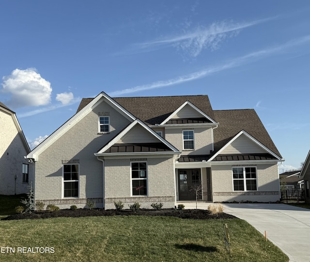 view of front of house with a front lawn, a standing seam roof, a shingled roof, metal roof, and brick siding