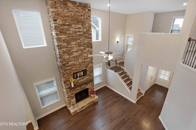 living room featuring ceiling fan, a fireplace, a high ceiling, and dark wood-type flooring