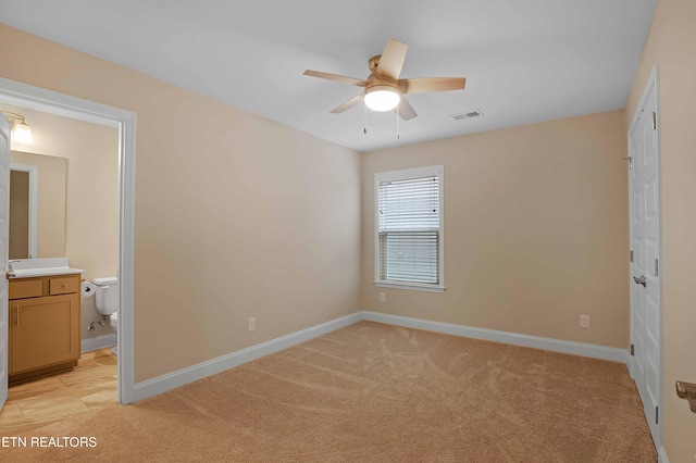 unfurnished bedroom featuring ceiling fan, light carpet, and connected bathroom