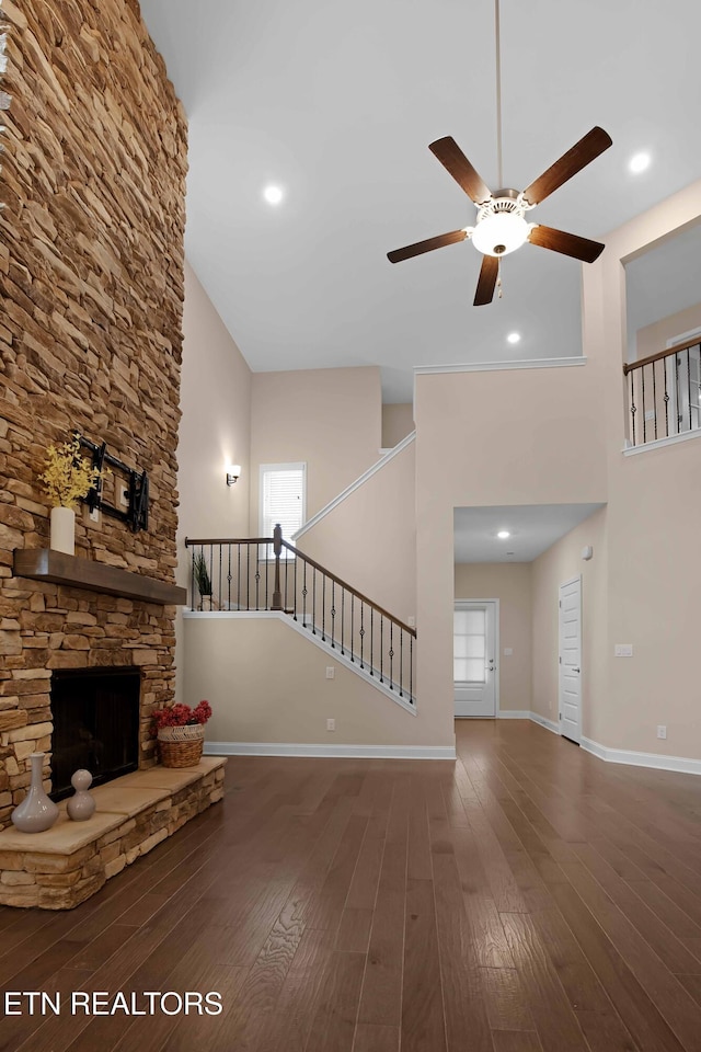 unfurnished living room featuring a fireplace, a high ceiling, dark hardwood / wood-style flooring, and ceiling fan