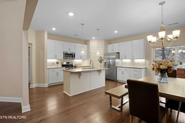 kitchen featuring a notable chandelier, a kitchen island with sink, white cabinets, decorative light fixtures, and stainless steel appliances