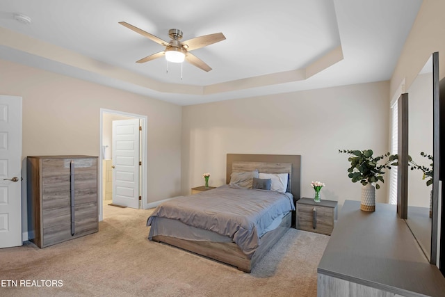 bedroom featuring ensuite bathroom, light colored carpet, a ceiling fan, baseboards, and a tray ceiling