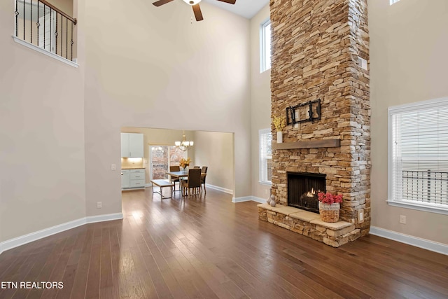 living room featuring ceiling fan with notable chandelier, a stone fireplace, wood finished floors, and baseboards