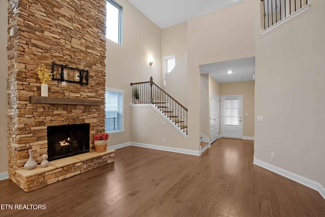 unfurnished living room featuring stairs, baseboards, wood finished floors, and a stone fireplace