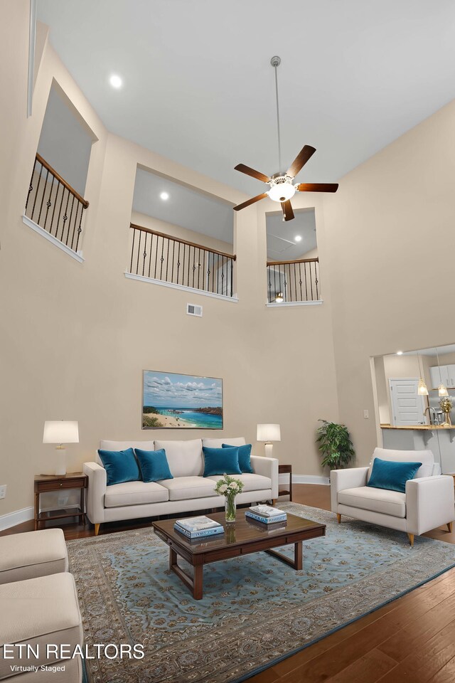 living room featuring a high ceiling, wood finished floors, visible vents, and a ceiling fan