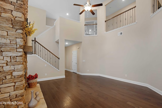 unfurnished living room featuring dark wood-style flooring, visible vents, baseboards, a ceiling fan, and stairway