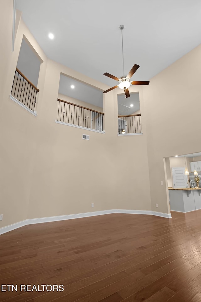 spare room with a high ceiling, visible vents, baseboards, a ceiling fan, and dark wood-style floors