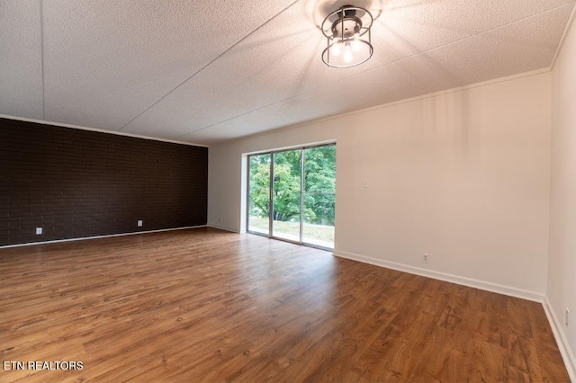 empty room featuring wood-type flooring, brick wall, and a textured ceiling