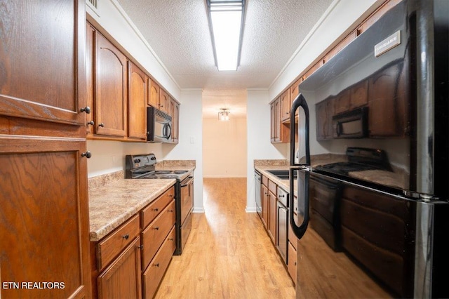 kitchen with a textured ceiling, crown molding, light wood-type flooring, and black appliances