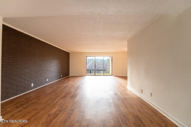 spare room featuring brick wall, a textured ceiling, and hardwood / wood-style floors