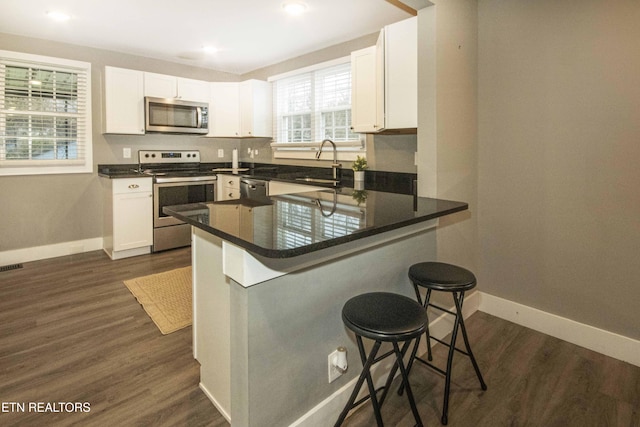 kitchen with a kitchen bar, white cabinetry, sink, and appliances with stainless steel finishes