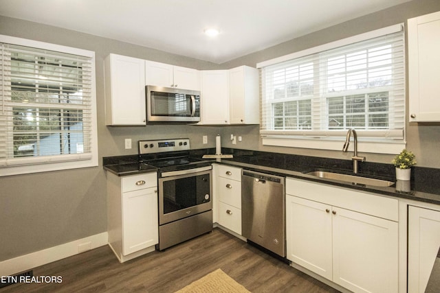 kitchen with sink, dark wood-type flooring, dark stone countertops, white cabinets, and appliances with stainless steel finishes