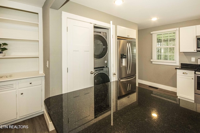 kitchen featuring white cabinets, stainless steel appliances, stacked washer / dryer, and dark stone countertops