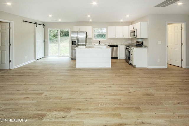 kitchen featuring white cabinets, a barn door, light hardwood / wood-style floors, a kitchen island, and stainless steel appliances