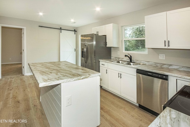 kitchen featuring stainless steel appliances, sink, a barn door, white cabinets, and a center island