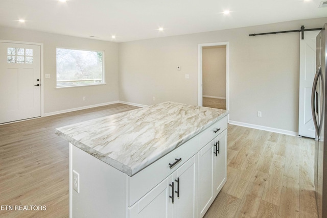 kitchen with light stone countertops, white cabinetry, a barn door, light hardwood / wood-style floors, and a kitchen island