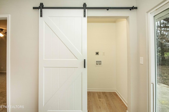 clothes washing area with electric dryer hookup, a barn door, light hardwood / wood-style flooring, and washer hookup