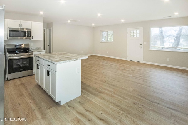 kitchen featuring light stone countertops, stainless steel appliances, a kitchen island, light hardwood / wood-style flooring, and white cabinets