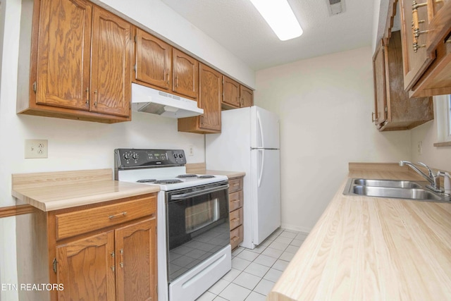 kitchen with a textured ceiling, sink, light tile patterned flooring, and white appliances