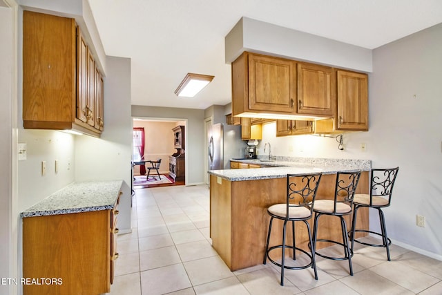 kitchen with kitchen peninsula, a kitchen breakfast bar, stainless steel refrigerator, and light stone countertops