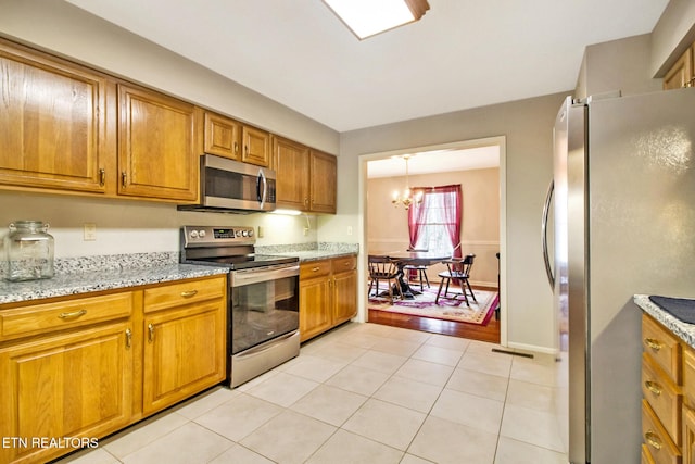 kitchen featuring pendant lighting, an inviting chandelier, light stone countertops, light tile patterned flooring, and stainless steel appliances