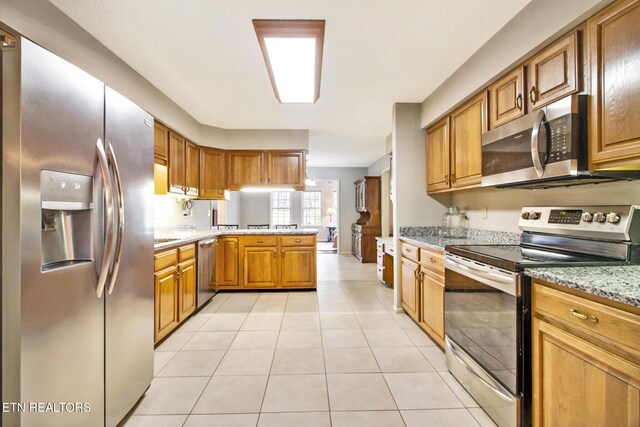 kitchen with light stone counters, light tile patterned floors, kitchen peninsula, and appliances with stainless steel finishes