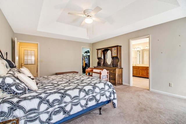 carpeted bedroom with ceiling fan, a spacious closet, a raised ceiling, ensuite bathroom, and a closet